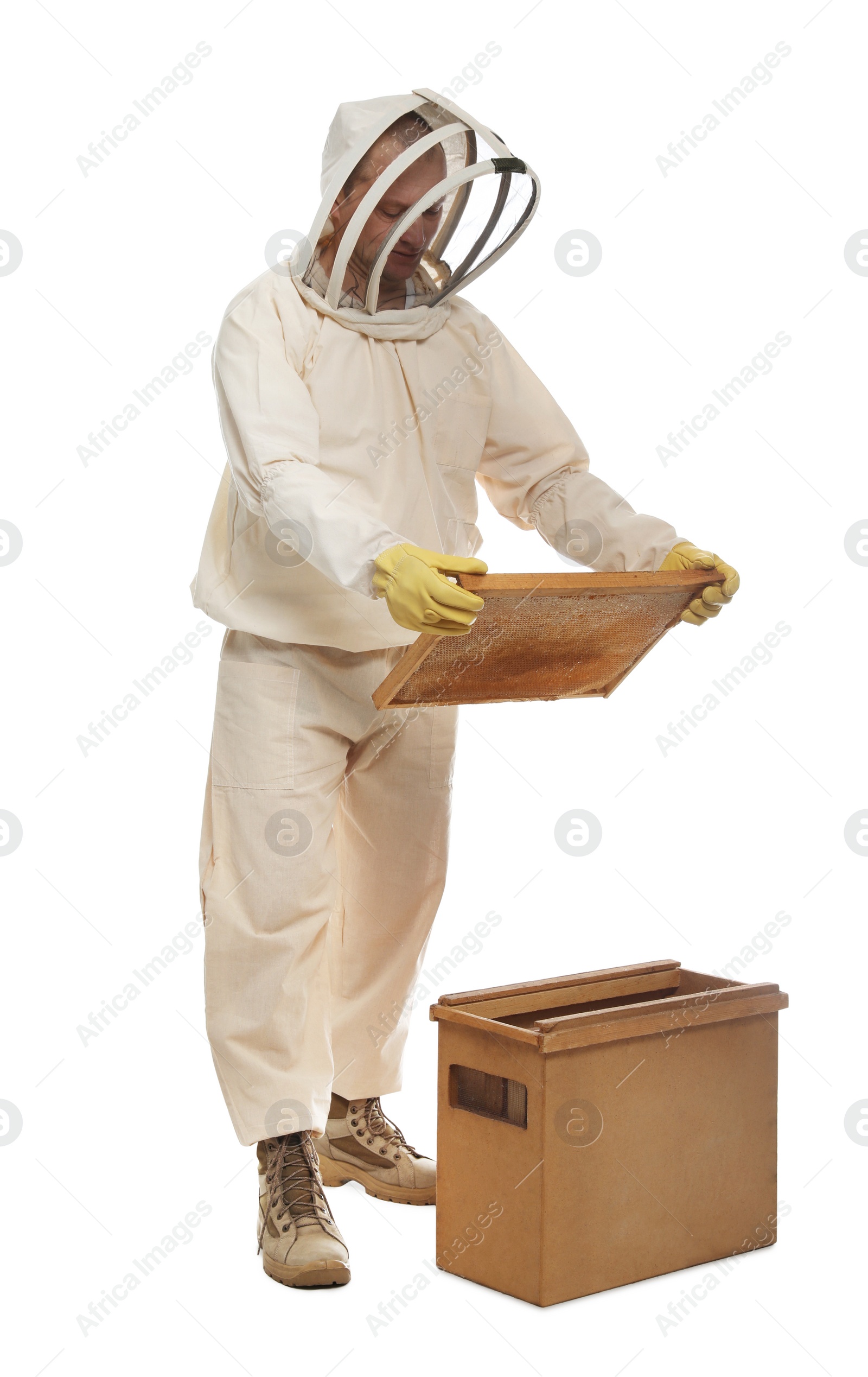 Photo of Beekeeper in uniform holding frame with honeycomb near wooden hive on white background