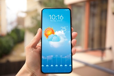 Woman checking weather using app on smartphone outdoors, closeup. Data and illustration of sun with cloud on screen