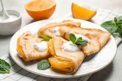 Photo of Delicious thin pancakes with oranges and cream on light table