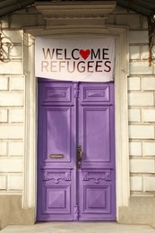 Image of Banner with phrase WELCOME REFUGEES hanging on closed vintage wooden door