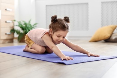 Photo of Little cute girl stretching herself on mat at home