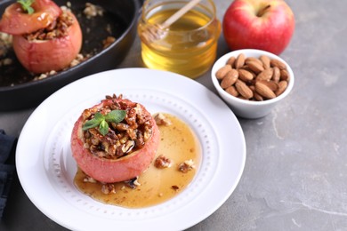 Photo of Tasty baked apples with nuts, honey and mint on gray textured table, closeup