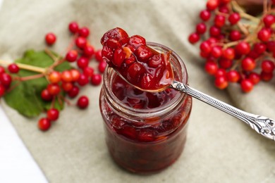 Photo of Spoon and jar with tasty viburnum jam on table
