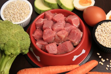 Raw meat in bowl and healthy products for pet on black background, closeup