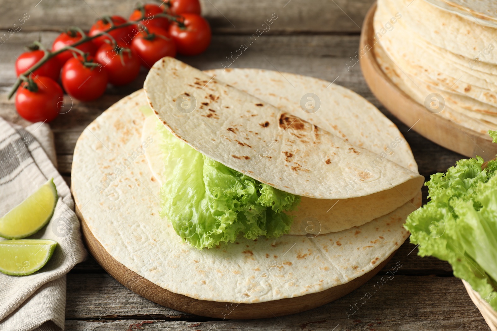 Photo of Tasty homemade tortillas, tomatoes, lime and lettuce on wooden table