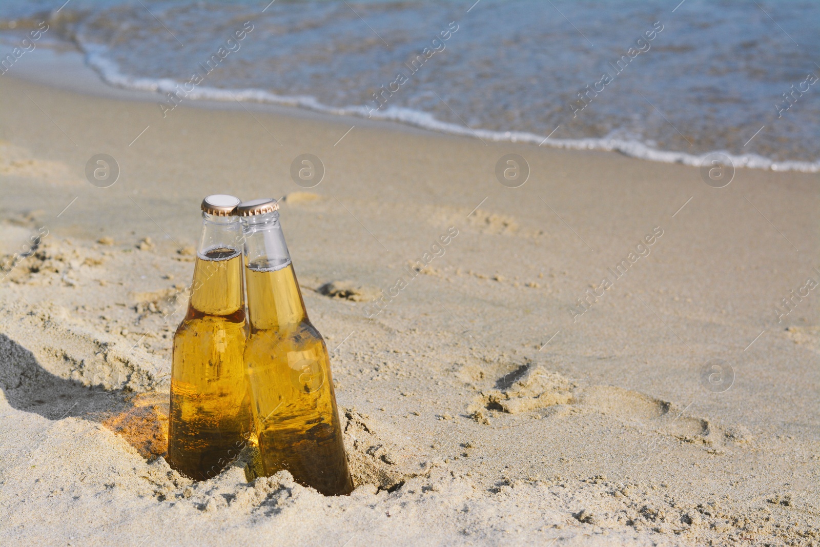 Photo of Bottles of cold beer on sandy beach near sea, space for text