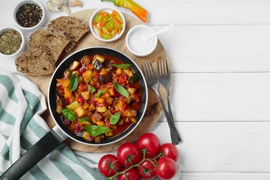 Photo of Frying pan with tasty ratatouille, ingredients and bread on white wooden table, flat lay. Space for text
