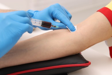 Doctor taking blood sample from patient with syringe at white table in hospital, closeup