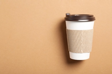 Takeaway paper coffee cup with cardboard sleeve on beige background, top view. Space for text