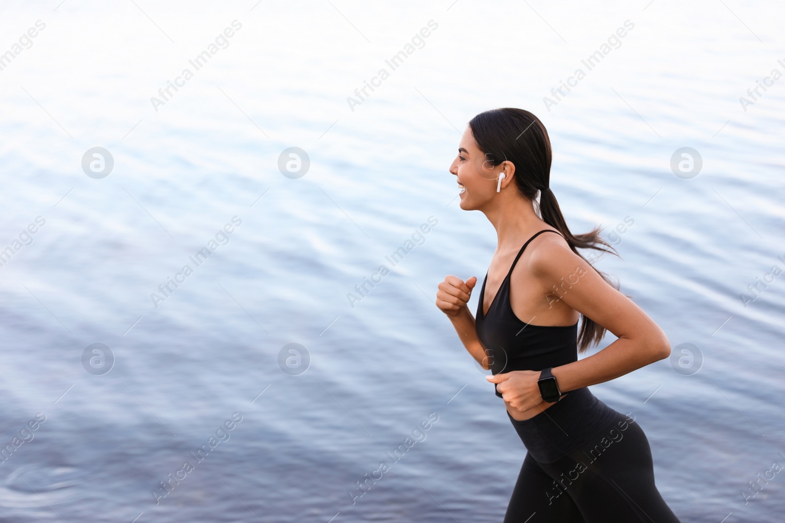 Photo of Young sportswoman with wireless earphones running near river