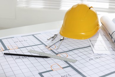 Photo of Construction drawings, safety hat and stationery on table in office