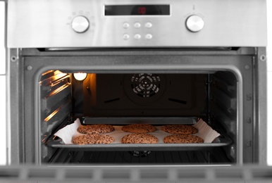 Photo of Open modern oven with freshly baked cookies on sheet in kitchen