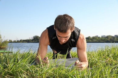 Photo of Sporty man doing plank exercise on green grass near river