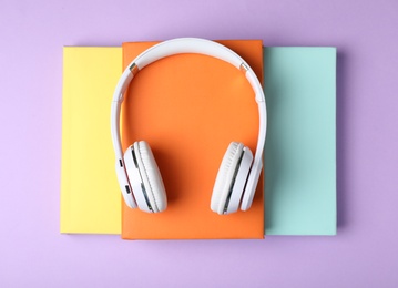 Modern headphones with hardcover books on color background, top view