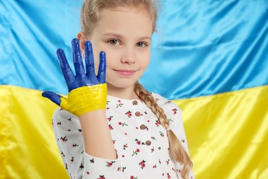 Little girl with paint on hand near Ukrainian flag