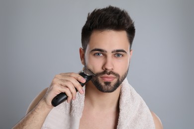 Photo of Handsome young man shaving with electric trimmer on grey background