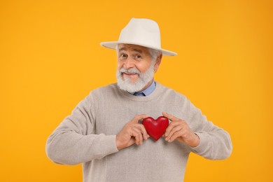 Photo of Senior man with red decorative heart on yellow background