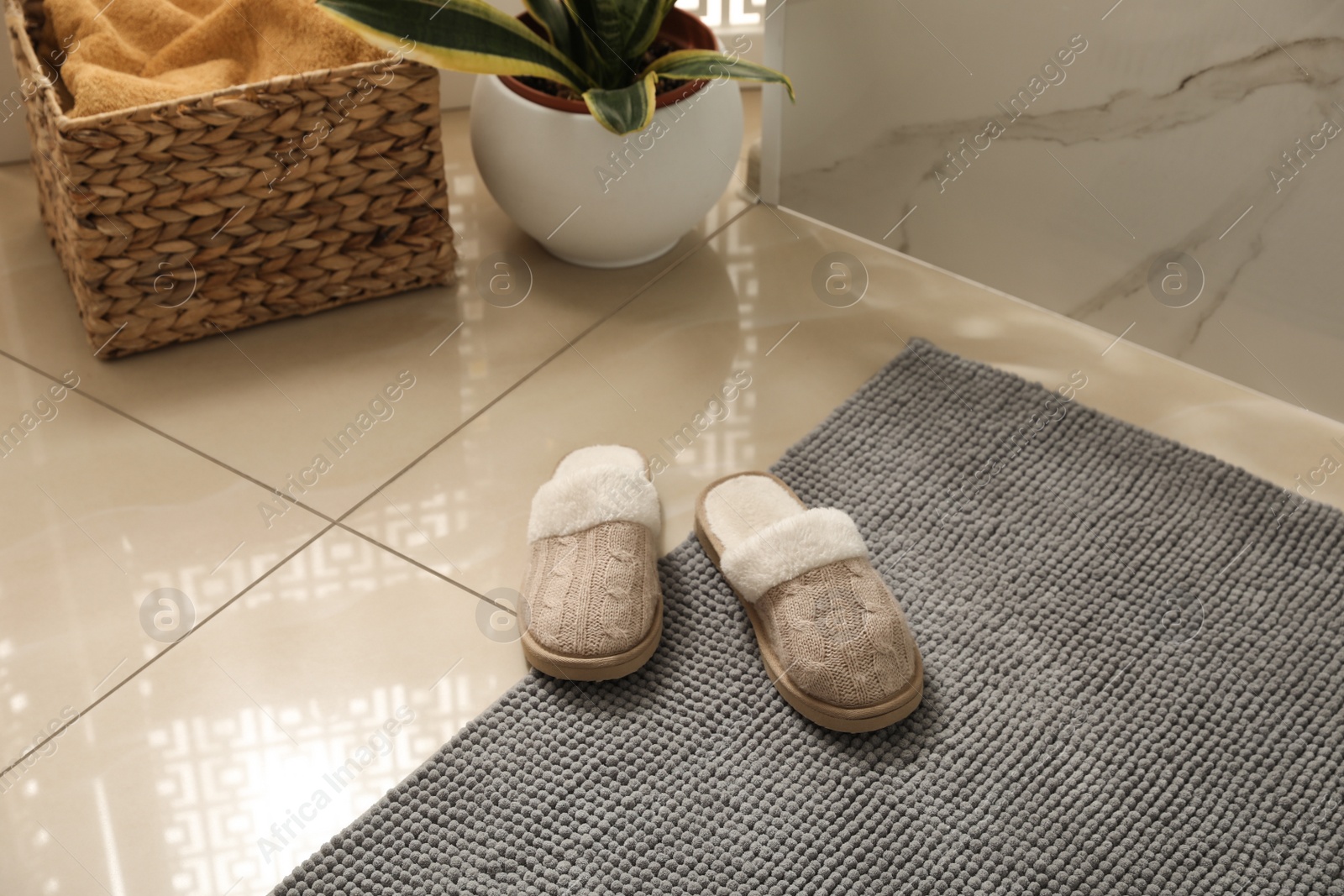 Photo of Soft grey bath mat and slippers on floor indoors