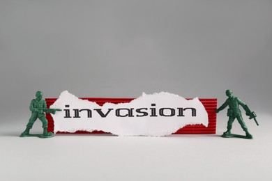Photo of Paper with word Invasion and toy soldiers on light grey background