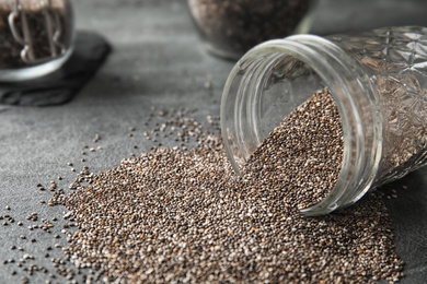 Photo of Glass jar and scattered chia seeds on grey table, closeup. Space for text