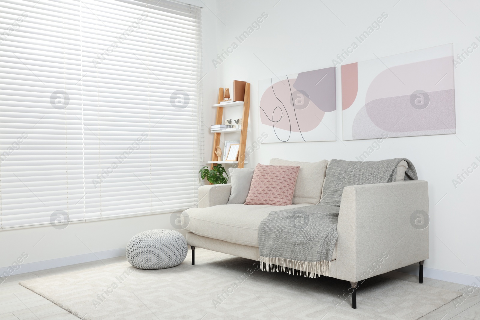 Photo of Stylish room interior with comfortable sofa, wooden shelf and pillows