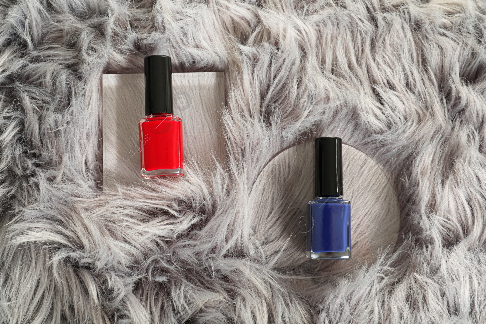 Photo of Bright nail polishes in bottles on grey faux fur, top view