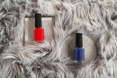 Photo of Bright nail polishes in bottles on grey faux fur, top view