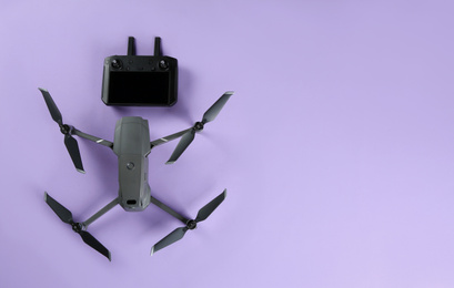 Photo of Modern drone with controller on lilac background, flat lay. Space for text