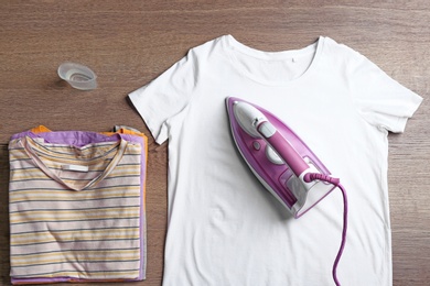 Photo of Flat lay composition with clothes and modern iron on wooden table