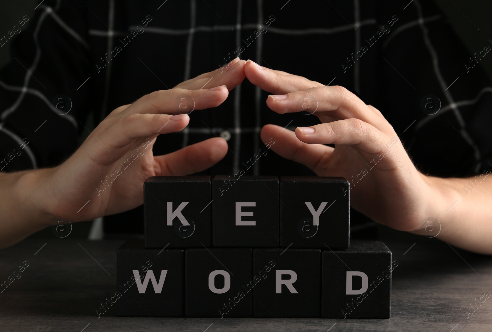 Photo of Woman demonstrating black cubes with word KEYWORD at grey table, closeup