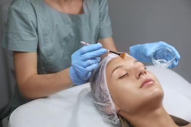 Photo of Cosmetologist applying chemical peel product on client's face in salon