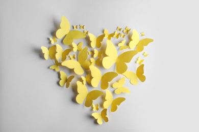 Photo of Heart shape made of yellow paper butterflies on white background, top view