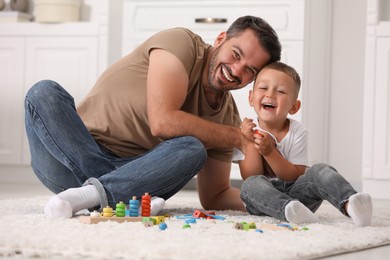 Photo of Motor skills development. Father and son playing with wooden pieces and string for threading activity on floor indoors