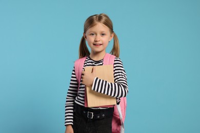 Photo of Happy schoolgirl with backpack and books on light blue background