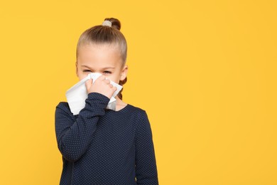 Photo of Sick girl blowing nose in tissue on yellow background, space for text. Cold symptoms