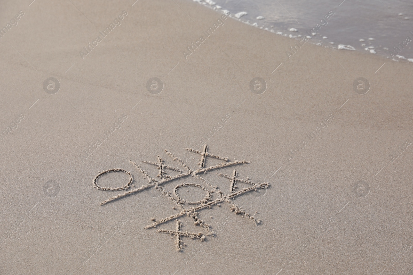 Photo of Tic tac toe game drawn on sand near sea, space for text