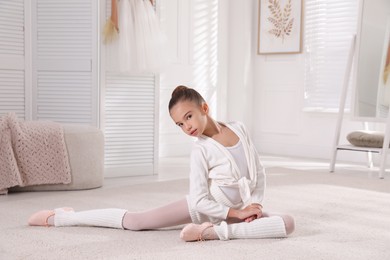 Photo of Little ballerina stretching on floor at home