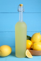 Photo of Bottle of tasty limoncello liqueur and lemons on light blue table