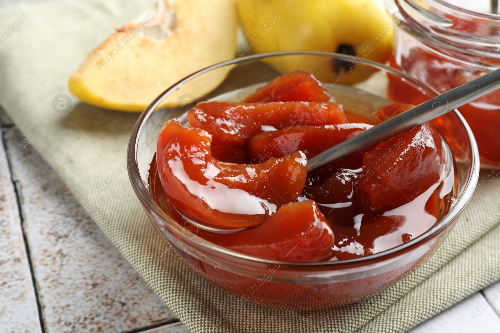 Photo of Tasty homemade quince jam in bowl on tiled table, closeup