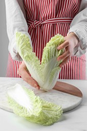 Photo of Woman separating leaf from fresh chinese cabbage at white table, closeup