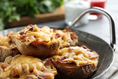 Photo of Frying pan of baked potatoes with cheese and bacon on table, closeup