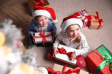 Photo of Cute little children with Christmas gifts on floor at home, above view