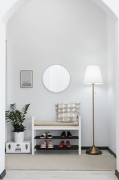 Stylish hallway room interior with bench, shoes and round mirror