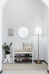 Photo of Stylish hallway room interior with bench, shoes and round mirror