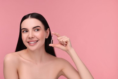 Photo of Beautiful young woman holding skincare ampoule on pink background