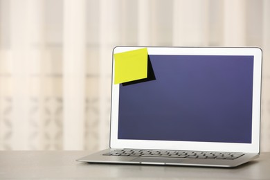 Laptop with empty sticky note on table indoors. Space for text