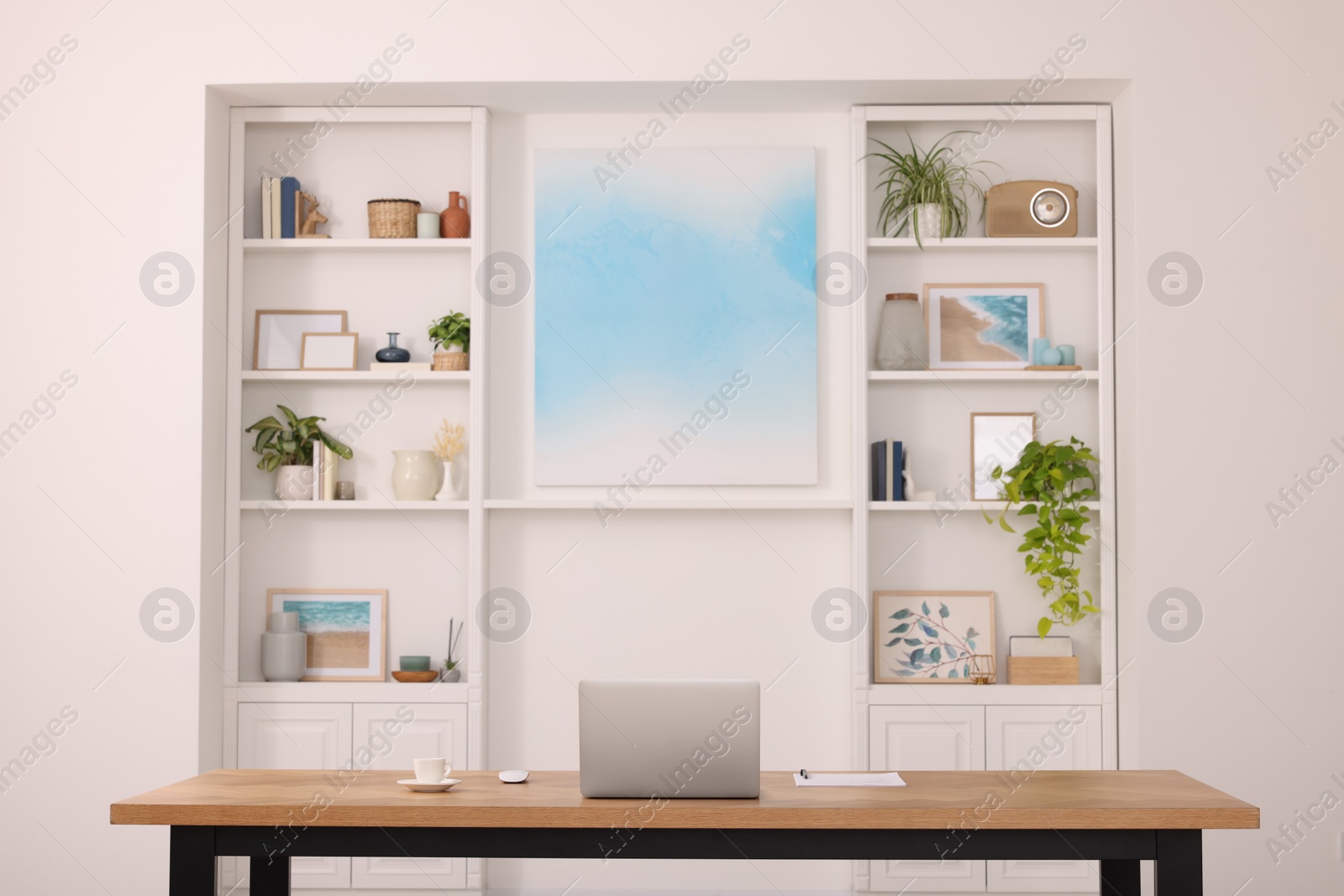 Photo of Interior design. Cosy workplace with laptop on wooden table near abstract picture between shelves