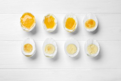 Different readiness stages of boiled chicken eggs on white wooden table, flat lay