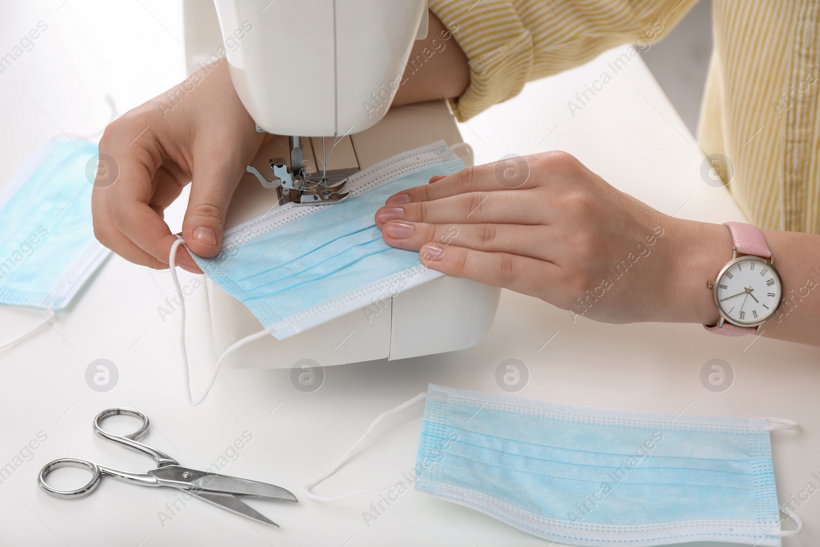 Photo of Woman making disposable mask with sewing machine at white table, closeup