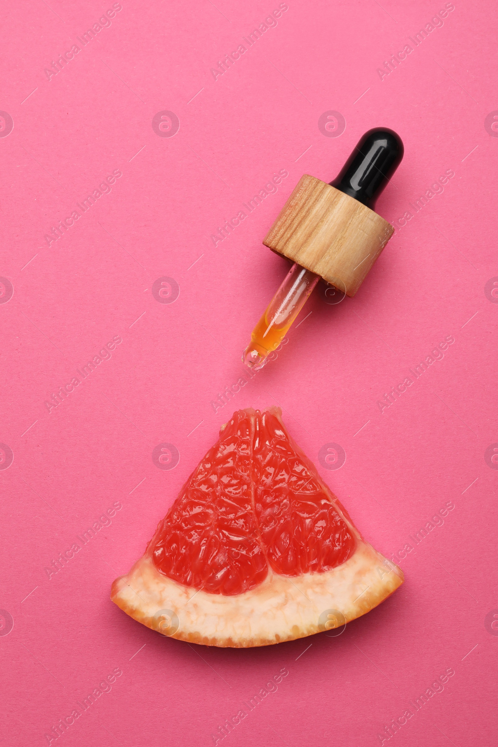 Photo of Pipette with citrus essential oil and fresh grapefruit slice on pink background, flat lay